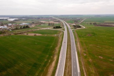 İlkbahar bulutlu bir günde kırsal alanda tarımsal alanlarla çevrili otobanın insansız hava aracı fotoğrafçılığı