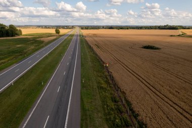 Yüksek yoğunluklu otoyol ile güneşli yaz günlerinde buğday tarlası arasında çit ören inşaat işçilerinin insansız hava aracı fotoğrafları..