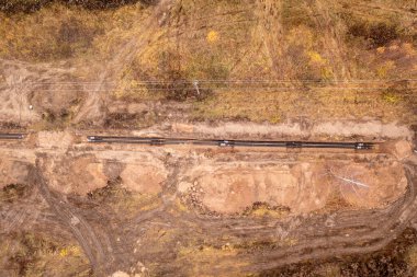 Kanalizasyon borusunun sonbahar bulutlu bir günde yol kenarındaki bir hendekte sürüklendiğini gösteren drone fotoğrafı.