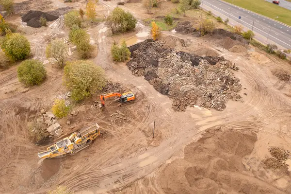 Drone photography of construction waste dumping site and machinery grinding it during autumn cloudy day