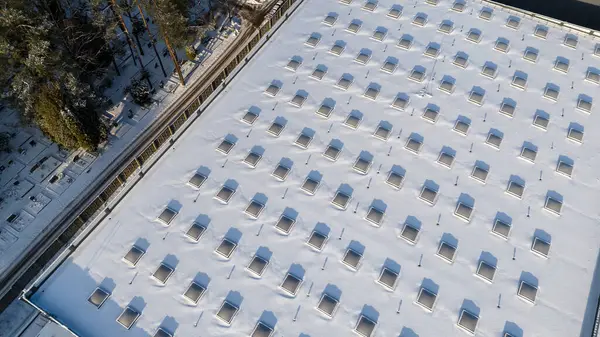 Drone photography of a large building rooftop with skylights covered by snow during winter sunny day