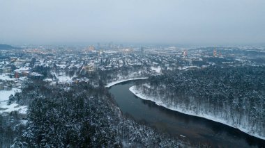 Ufukta bulutlu bir kış günü, kar ve şehir manzarası ile kaplı nehir boyunca akan drone fotoğrafçılığı
