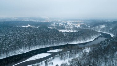 Ufukta bulutlu bir kış günü, kar ve şehir manzarası ile kaplı nehir boyunca akan drone fotoğrafçılığı