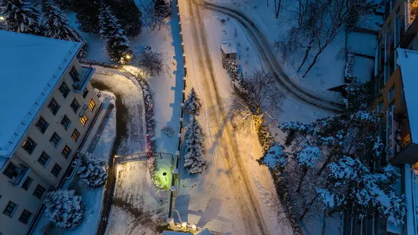 Kışın bulutlu akşamlarda binalar arasında karla kaplı caddenin drone fotoğrafçılığı