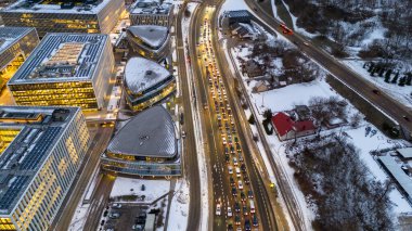 Ana caddenin sabah trafiğinin drone fotoğrafları kış bulutlu bir günde karla kaplı ofis binalarının yakınına gidiyor.