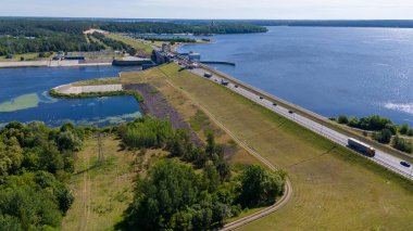 Güneşli yaz gününde barajın üzerinden geçen bir su barajının, ormanın ve yolun insansız hava aracı fotoğrafları.