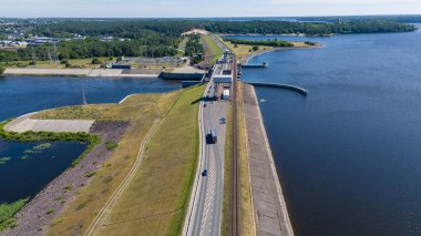 Güneşli yaz gününde barajın üzerinden geçen bir su barajının, ormanın ve yolun insansız hava aracı fotoğrafları.
