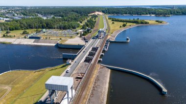 Güneşli yaz gününde barajın üzerinden geçen bir su barajının, ormanın ve yolun insansız hava aracı fotoğrafları.