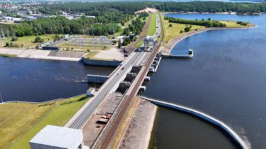 Güneşli yaz gününde barajın üzerinden geçen bir su barajının, ormanın ve yolun insansız hava aracı görüntüleri.