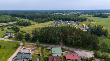 Güneşli yaz günlerinde etrafı ormanla çevrili küçük kasaba ve elektrik hatlarının drone fotoğrafları.