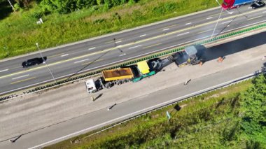 Otoyoldaki bir inşaat alanının havadan çekilmiş görüntüleri. İçinde büyük bir asfalt döşeme makinesi ve işçiler var. Sitede kısmen tamamlanmış bir köprü veya yol bölümü gösteriliyor.
