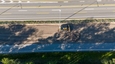 Açık mavi gökyüzünün altında yoğun yeşil ormanlarla çevrili bir otoyolun havadan görünüşü. Yol, doğa ve altyapının bir karışımını sergileyen, görünür araçlarla yapım aşamasında..