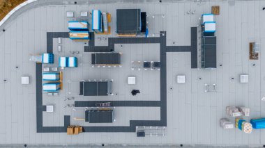 Çeşitli havalandırma ve havalandırma sistemlerinin bulunduğu ticari bir binanın çatısı görüntüsü. Düz çatı çoğunlukla gri ve siyah yollar var..