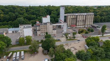 Büyük siloların, tren raylarının ve yeşilliklerle çevrili yük vagonlarının bulunduğu bir sanayi bölgesinin havadan görüntüsü. Sahne, doğa ve endüstrinin kesişimlerini yakalar..