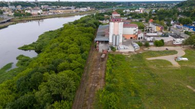 Büyük siloların, tren raylarının ve yeşilliklerle çevrili yük vagonlarının bulunduğu bir sanayi bölgesinin havadan görüntüsü. Sahne, doğa ve endüstrinin kesişimlerini yakalar..