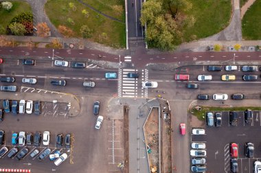 Kalabalık bir kavşağın birden fazla şeridi olan hava görüntüsü. Çevredeki alanlar arasında yeşil ağaçlar ve park halindeki arabaların olduğu bir otopark yer alıyor. İnşaat işi yolun bir tarafında belli..