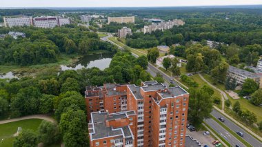 Konut ve apartman binalarının karışımının yer aldığı bir banliyö bölgesinin havadan görüntüsü. Manzara, yeşillik ve kentsel yapılar, konut ve apartmanların karışımından oluşan bir banliyö bölgesinin havadan görünüşünü içeriyor. Toprak