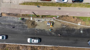 Ağır makineler ve işçilerle dolu bir yol şantiyesinin havadan görüntüsü. Teçhizatta küçük bir yükleyici ve çeşitli araçlar vardır. Yol yüzeyi tamir ediliyor..