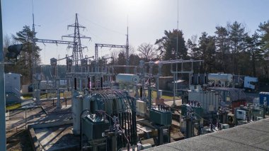 Çeşitli trafolar, devre kesiciler ve elektrik hatlarının yer aldığı endüstriyel bir elektrik santrali. Sahne açık gökyüzü ve güneş ışığı ile açılır..