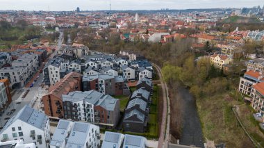 Modern ve geleneksel mimarinin bir karışımını içeren bir şehir manzarasının havadan görünüşü. Şehir çevresinin doğal güzelliğini artıran bir nehir sahnenin içinden akar..
