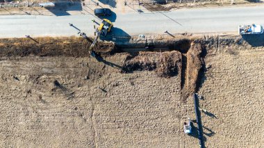 Aerial view of construction site with excavators digging a trench for a pipe near a road. clipart