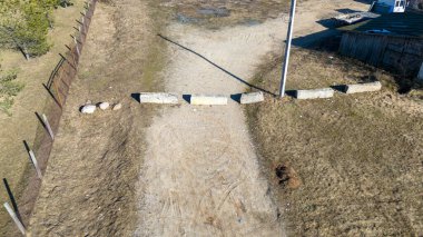 Beton bariyerler, çitler ve küçük bir bina ile engellenmiş kırsal toprak bir yolun havadan görünüşü .