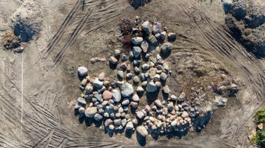 Toprak bir yüzey üzerinde çeşitli büyüklükteki kayaların yer aldığı bir depolama alanının hava görüntüsü. Civarda lastik izleri var. Son zamanlardaki hareketliliği gösteriyor..