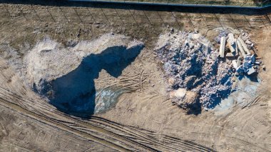 Toprak bir yüzey üzerinde çeşitli büyüklükteki kayaların yer aldığı bir depolama alanının hava görüntüsü. Civarda lastik izleri var. Son zamanlardaki hareketliliği gösteriyor..