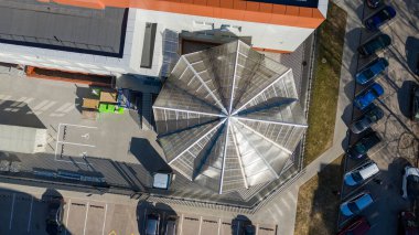 Park halindeki arabalar ve kaldırımlarla çevrili, eşsiz geometrik cam çatılı modern bir binanın havadan görünüşü..