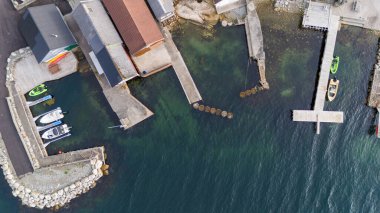 Rıhtımlı birkaç teknesi olan bir marinanın havadan görüntüsü. Su sakin ve berrak, deniz yatağını ortaya çıkarıyor. Çevresindeki yapılar renkli binalar ve ahşap rıhtımlar, resim gibi bir manzara yaratıyorlar..