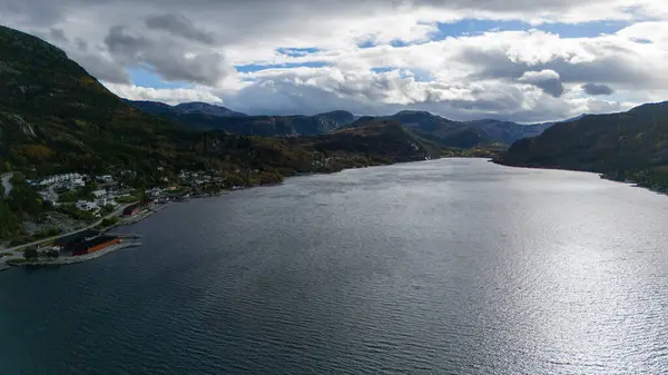 Norveç fiyortlarında sakin bir su kütlesi ve uzak adalara bakan sonbahar yapraklarıyla çevrili manzaralı kıyı köyü manzarası..