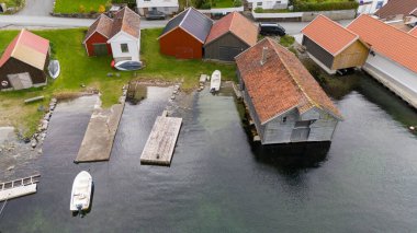Limanı, park edilmiş arabaları ve konut binaları olan küçük bir sahil köyünün havadan görünüşü. Limanda küçük bir rıhtım ve bir tekne bulunurken, çevre bölgede yollar ve yeşillikler yer alıyor..
