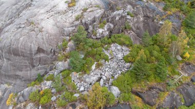 Bereketli yeşil ormanların, kayalık uçurumların ve çeşitli sonbahar yapraklarının yer aldığı dağlık bir manzaranın manzarası. Gökyüzü bulutlu, doğal güzelliğe dramatik bir atmosfer ekliyor..