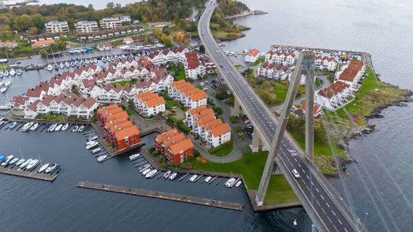 Kırmızı çatıları olan modern yerleşim binalarının bulunduğu kıyı kasabasının havadan görünüşü, tekneli bir marina ve su üzerindeki araziyi birbirine bağlayan bir köprü..