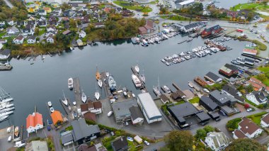 İskan evleri ve yeşilliklerle çevrili tekneleri olan bir marinanın havadan görüntüsü..