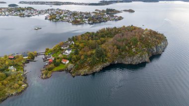 Sakin sularla çevrili yemyeşil yemyeşil bir adanın bulunduğu kıyı manzarası. Sahilde renkli evleri olan küçük bir köy görülebiliyor ve güzel bir manzara yaratıyor..
