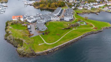 Modern evler, yeşil çimenler ve su ve kayalık kıyılarla çevrili bir oyun alanı olan küçük bir sahil köyünün havadan görünüşü..