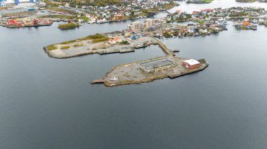 Sakin sularla çevrili sanayi binaları ve rıhtımı olan küçük bir adanın havadan görünüşü ve yakındaki bir sahil kasabası..