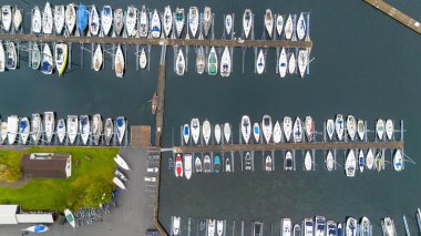 Paralel sıralara kenetlenmiş sayısız yelkenlisi olan bir marinanın havadan görüntüsü..