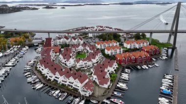 Kırmızı çatılı evleri, marinası ve köprüsü olan bir sahil köyünün havadan görüntüsü..