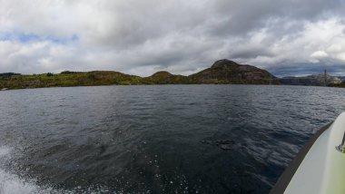 Sakin bir göl manzarası. Arka planda bulutlu bir gökyüzünün altında dağlık bir manzara..