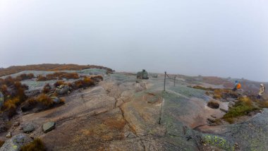 Kayalık arazi ve yürüyüşçülerle sisli dağ manzarası.