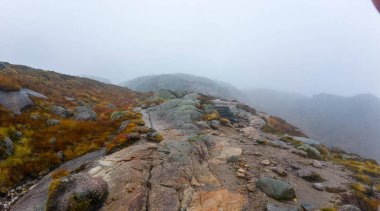 Kayalık arazi ve seyrek bitki örtüsüyle puslu dağ manzarası.
