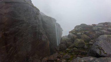 Sis ile çevrili kayalıklar arasında çağlayan bir şelalesi olan sisli bir manzara..