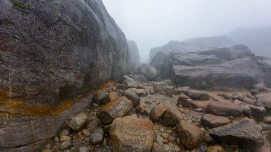 Büyük kayalar ve kayaların arasından akan küçük bir dereyle puslu dağ manzarası..