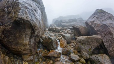 Büyük kayalar ve kayaların arasından akan küçük bir dereyle puslu dağ manzarası..
