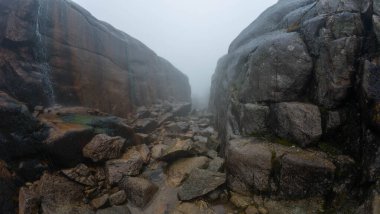 Sert kaya oluşumları ve dağınık kayalarla sisli bir dağ geçidi..