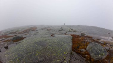 Kayalık arazi ve küçük su birikintileriyle sisli dağ zirvesi.