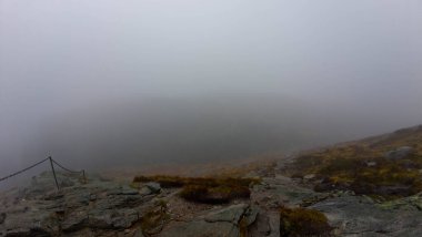 Kayalık arazi ve seyrek bitki örtüsüyle sisli bir dağ manzarası.