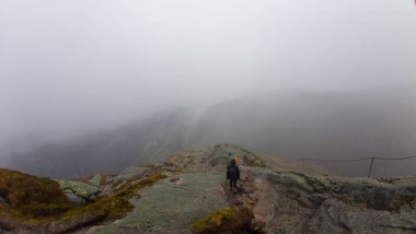 Kayalık bir patika boyunca yürüyen yürüyüşçülerle sisli bir dağ manzarası..